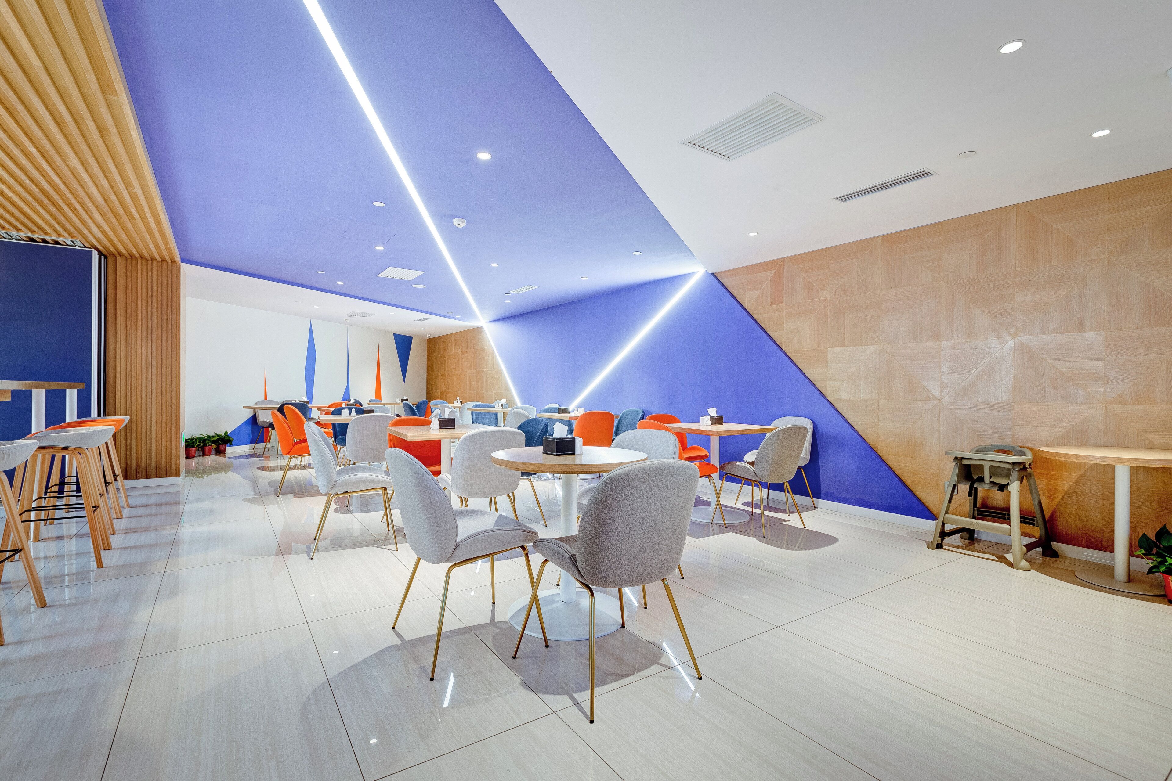 A modern interior with a blue ceiling, white walls, and a mix of round and square tables with chairs.