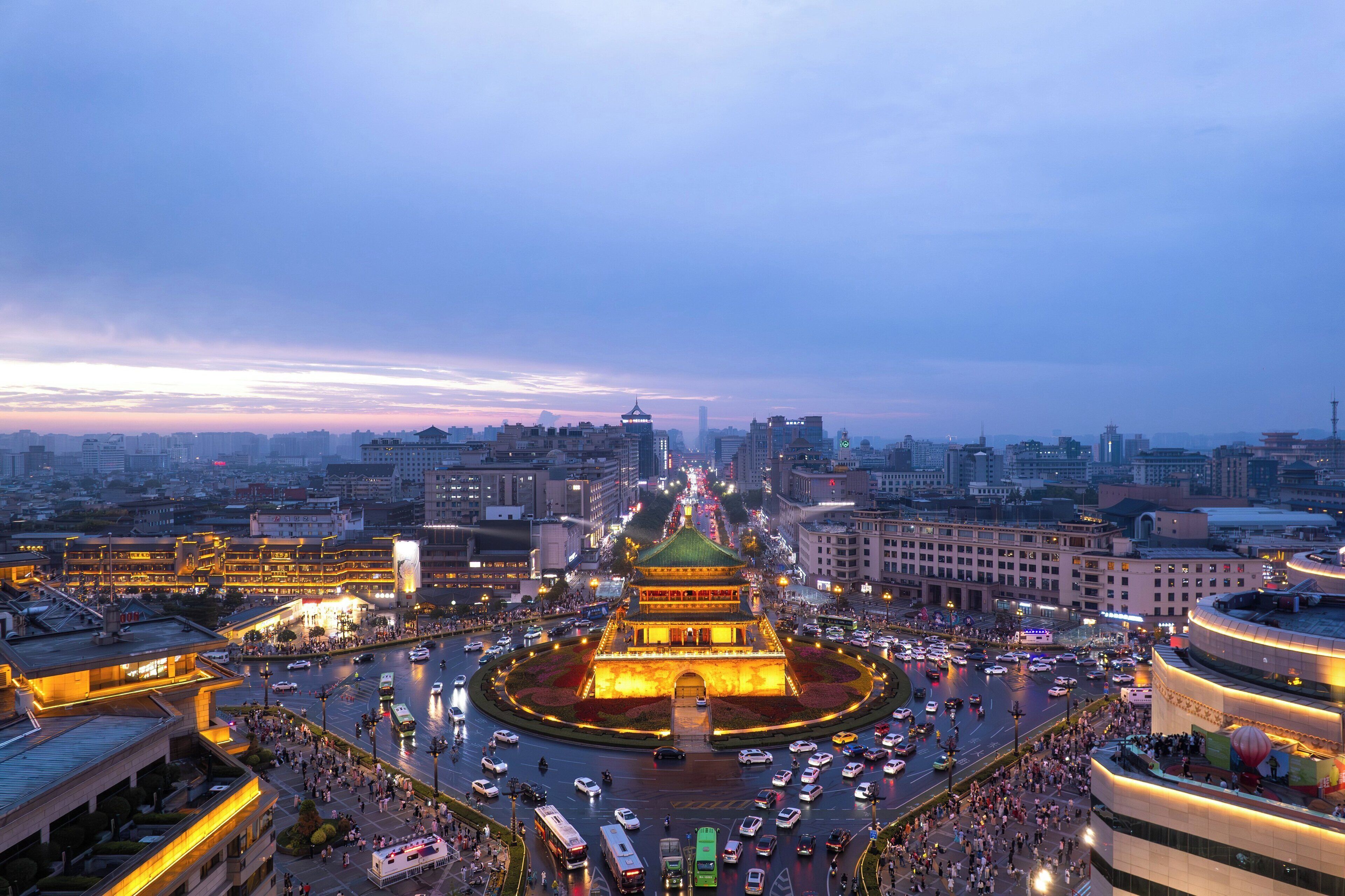 A cityscape with a prominent traditional building in the center, surrounded by modern buildings and a busy intersection.