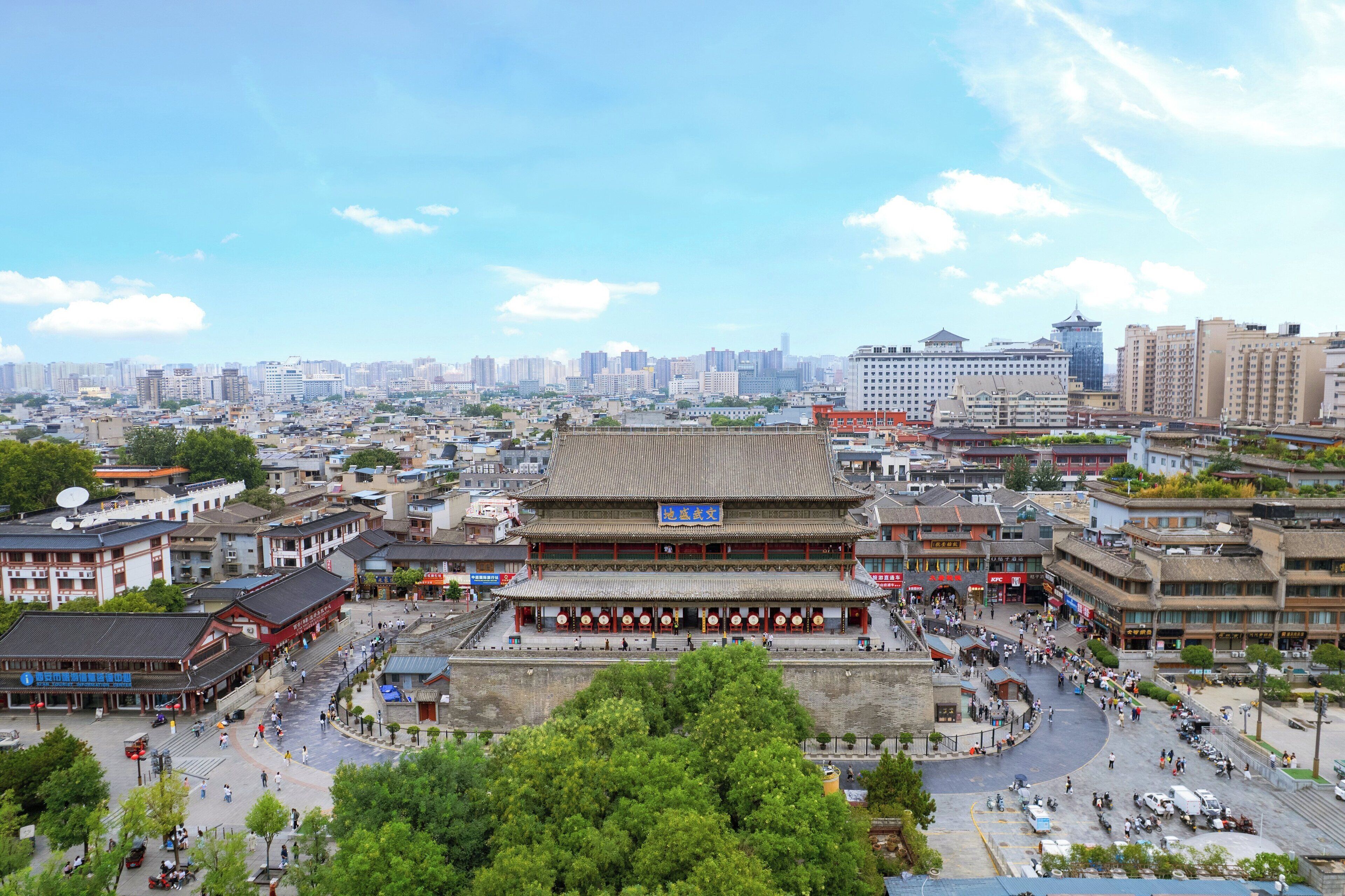 A traditional building with a tiled roof and multiple floors, surrounded by a bustling urban area with modern high-rise buildings in the background.