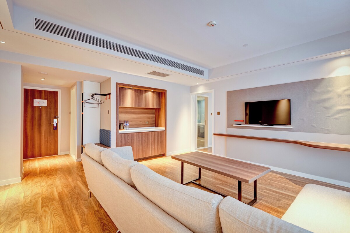 A modern living room with a sofa, a wooden table, and a television mounted on the wall.