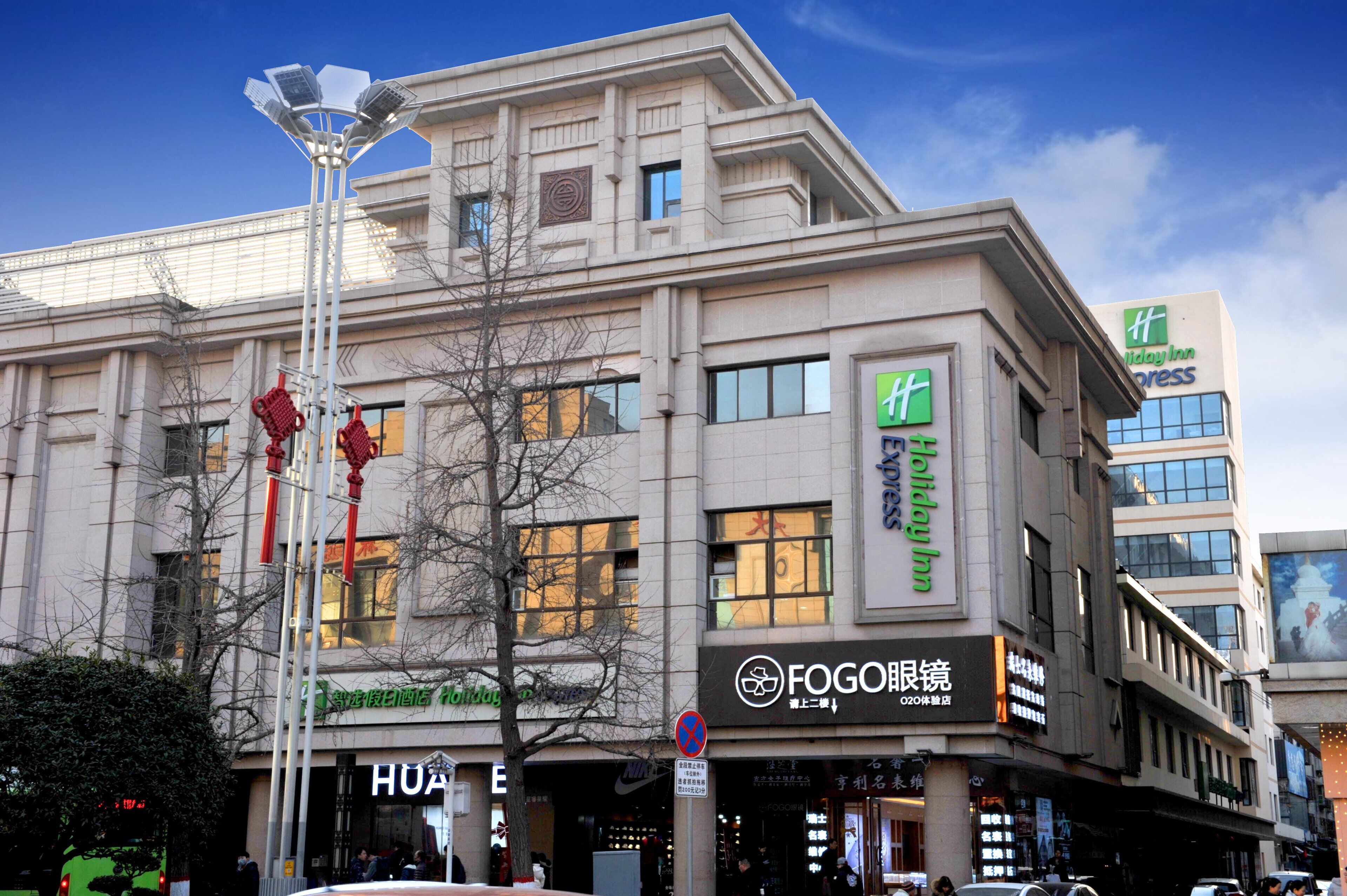 Een meerlaags gebouw met een Holiday Inn Express bord, een Fogo restaurant en een Huawei winkel.