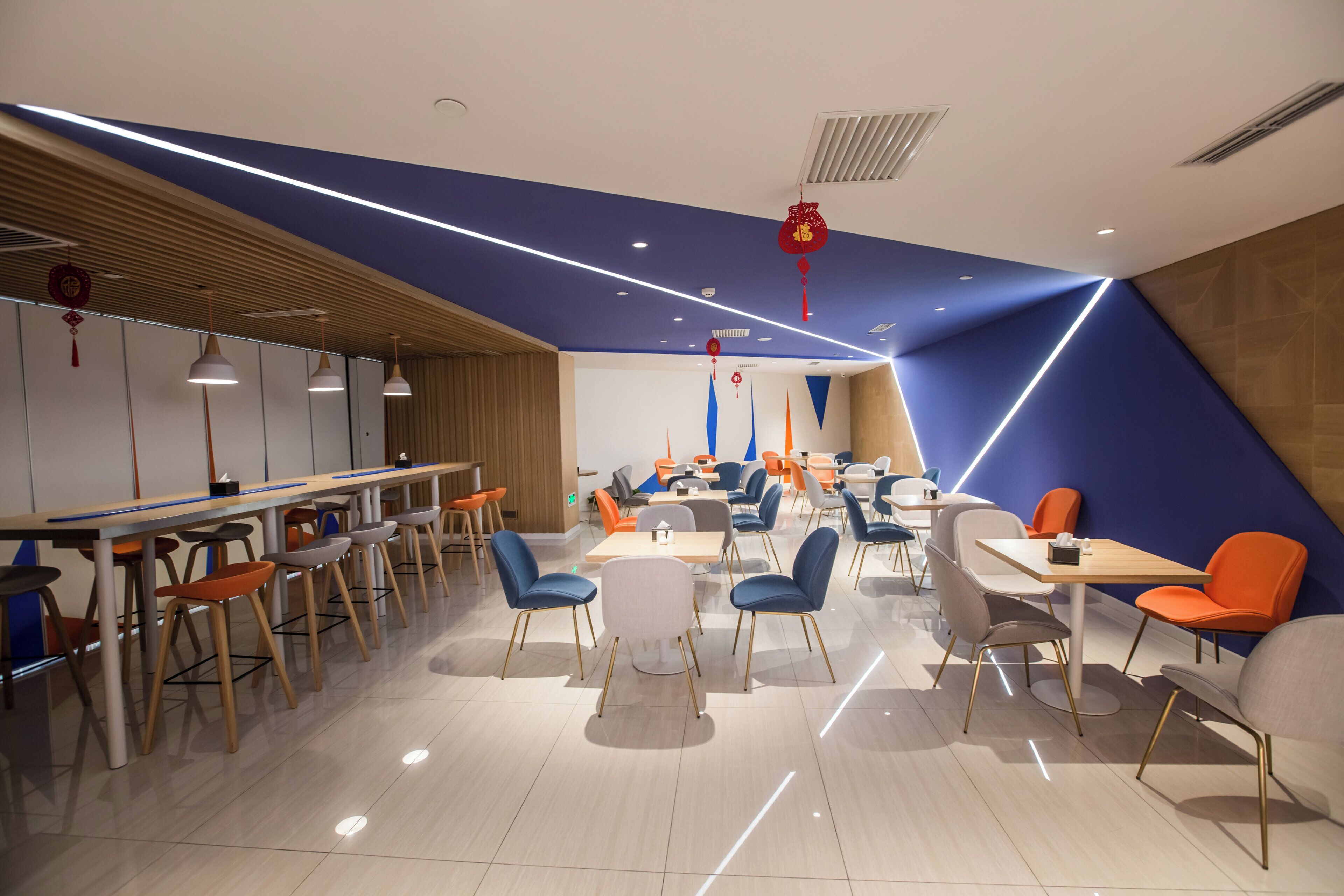 A modern dining area with multiple tables and chairs, a wooden accent wall, and a blue ceiling design.