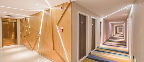 A modern hotel corridor with a reflective floor, wooden panel walls, and a striped carpet.