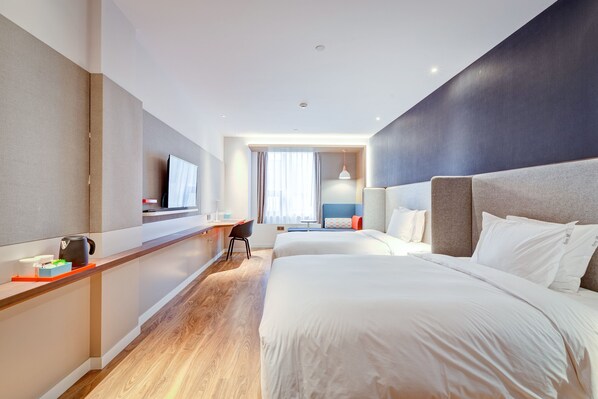 Ein modernes Hotelzimmer mit einem großen Bett, einem Schreibtisch mit Wasserkocher und einem Fernseher.