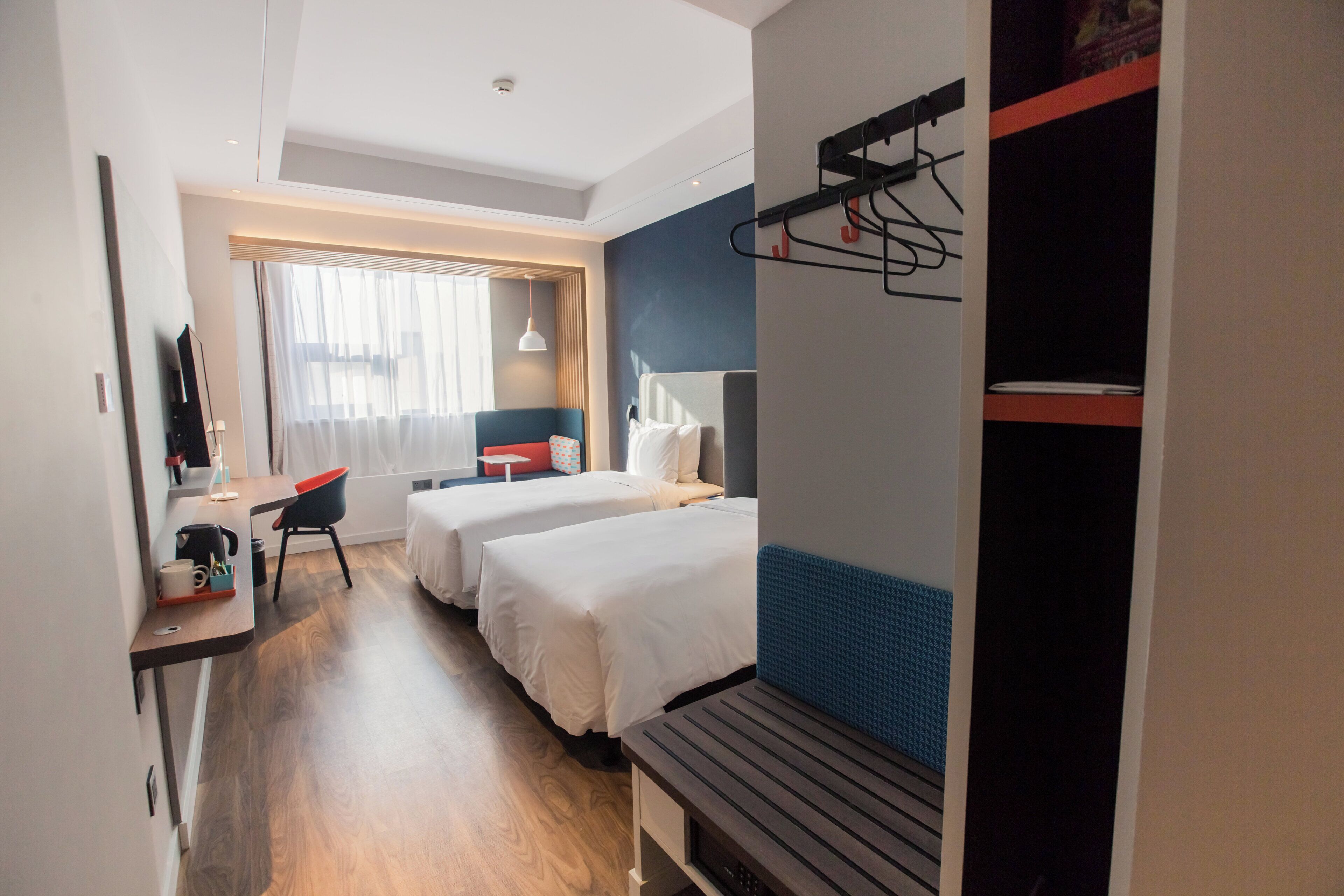 Une chambre d’hôtel avec deux lits, un bureau, une chaise, un banc et une armoire.