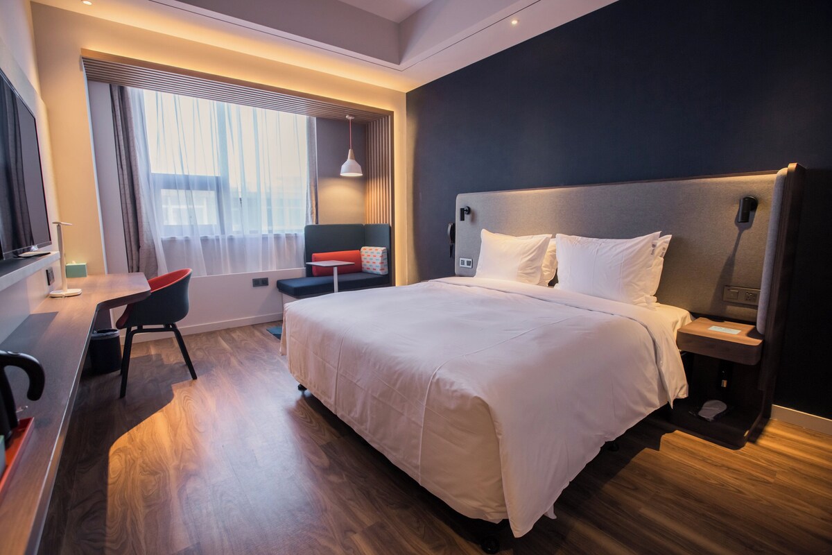 A modern hotel room with a large bed, a desk, and a chair.