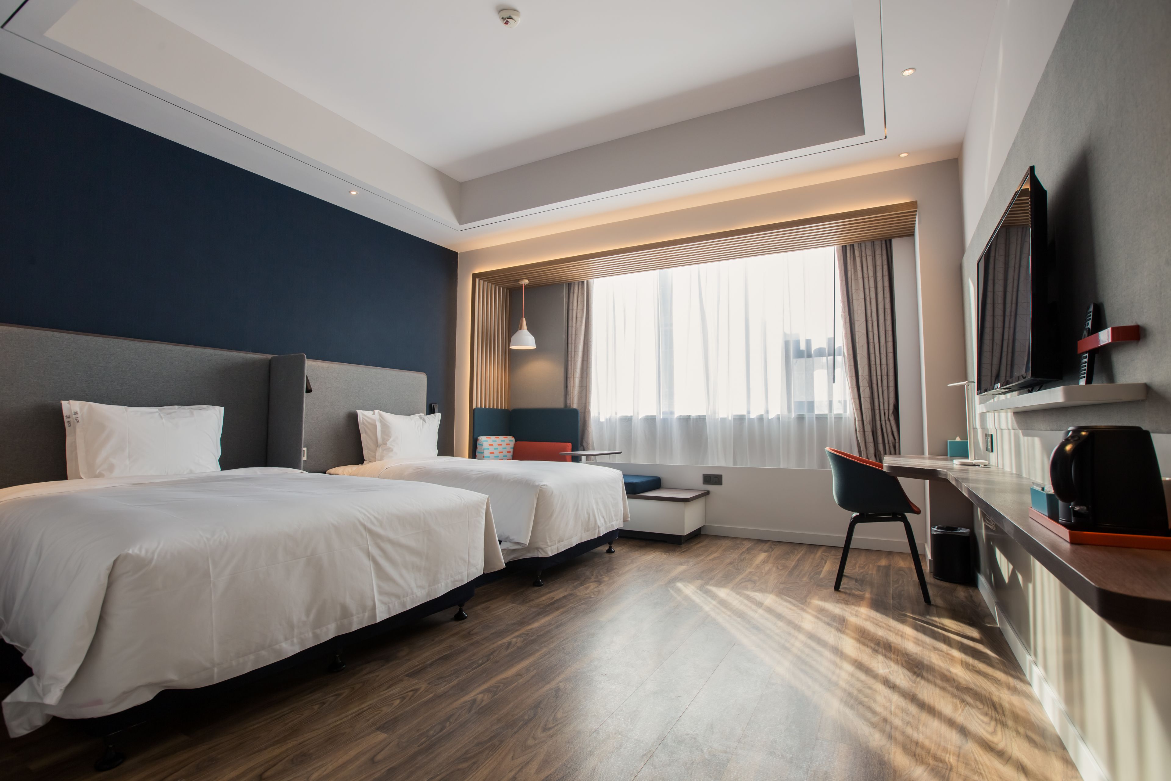 A hotel room with two beds, a desk, a chair, a TV, and a window with curtains.
