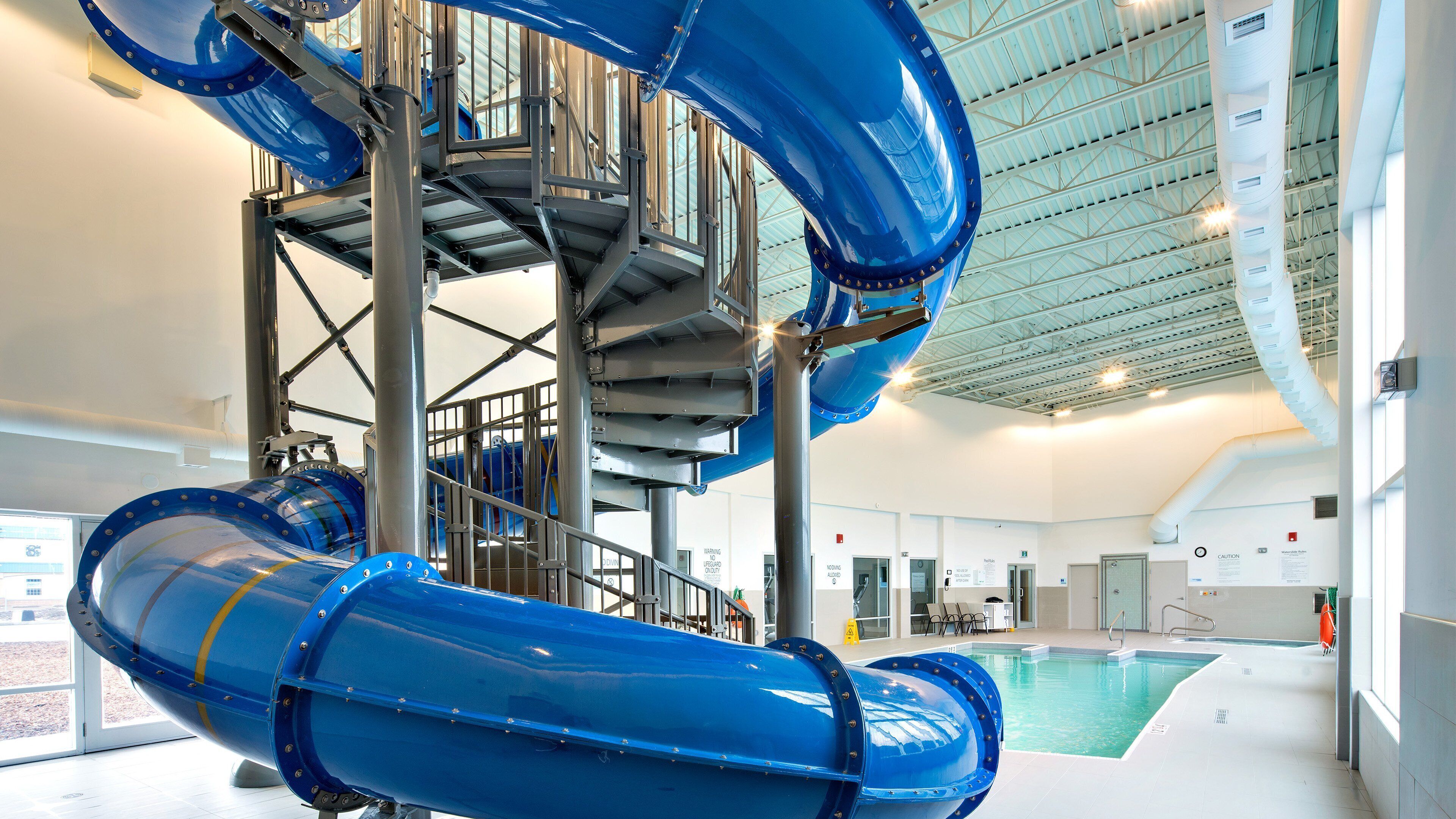 Une structure de toboggan aquatique comprenant un escalier en spirale, une piscine intérieure et une signalisation de sécurité.