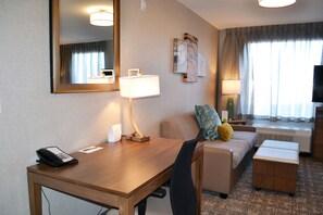 A hotel room with a wooden desk, a telephone, a lamp, a sofa, a television, and a window with curtains. - Staybridge Suites Red Deer North  by IHG (Red Deer)