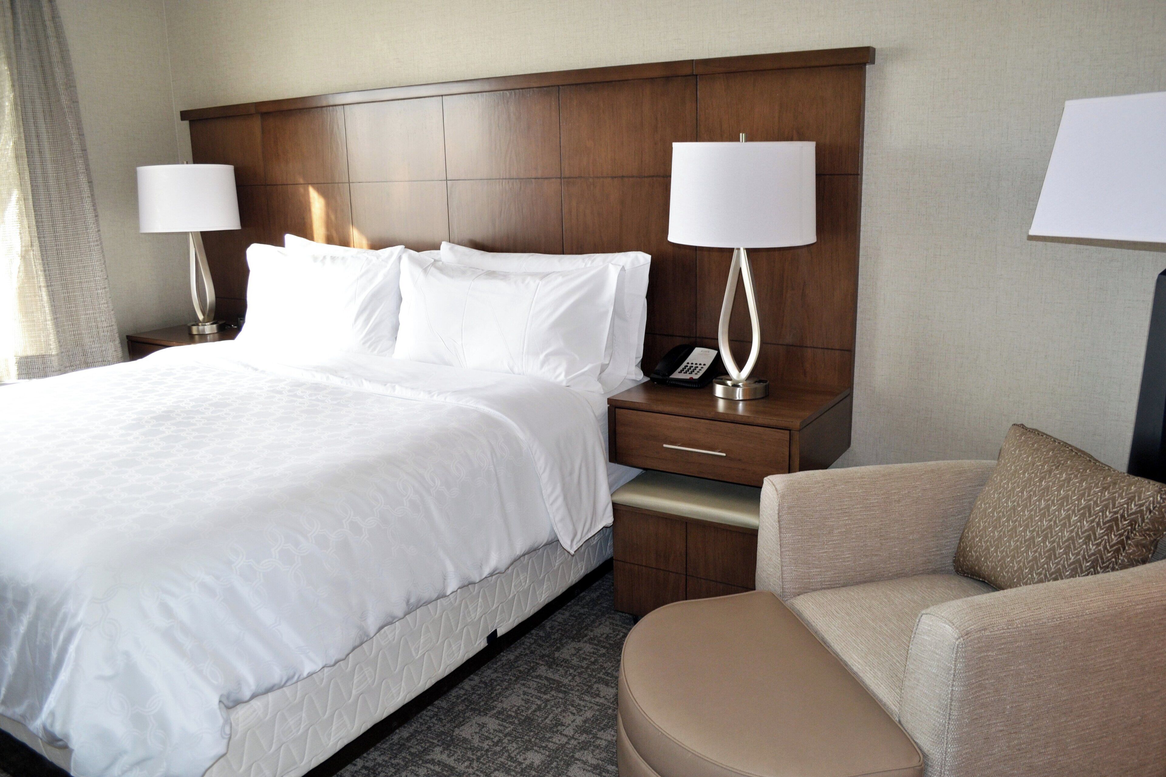 Habitación de hotel con una cama grande, dos mesitas de noche con lámparas, una silla y un tocador con teléfono.