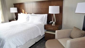 Habitación de hotel con una cama grande, dos mesitas de noche con lámparas, una silla y un tocador con teléfono.