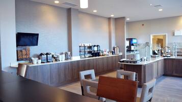 A modern hotel lobby with a reception desk, seating area, and a coffee station.