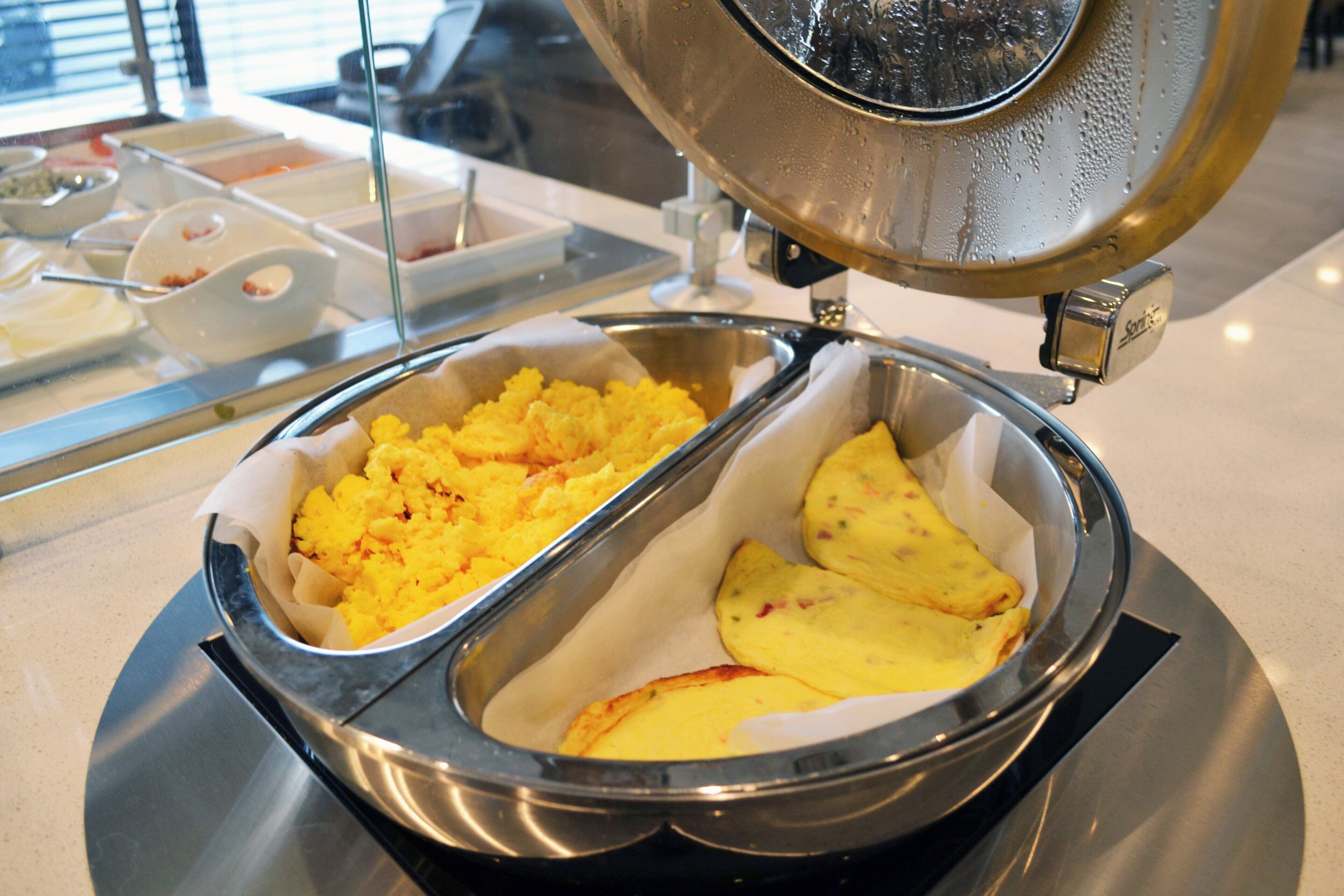 A buffet with a variety of food items, including scrambled eggs and baked potatoes.