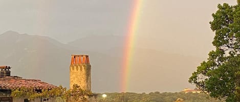 Paisaje rural con edificios tradicionales, una chimenea destacada y un arcoíris al fondo.