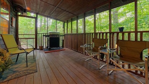 Une véranda couverte avec un plancher en bois, des chaises en métal, une petite table et un barbecue.