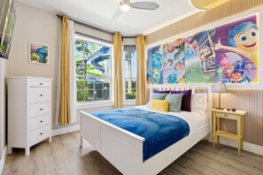 Un dormitorio con cama, mesita de noche, cómoda, ventana con cortinas y un mural en la pared.