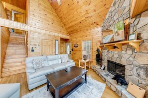Ein gemütliches Blockhaus-Interieur mit Kamin aus Stein, einer Couch und einer Treppe.
