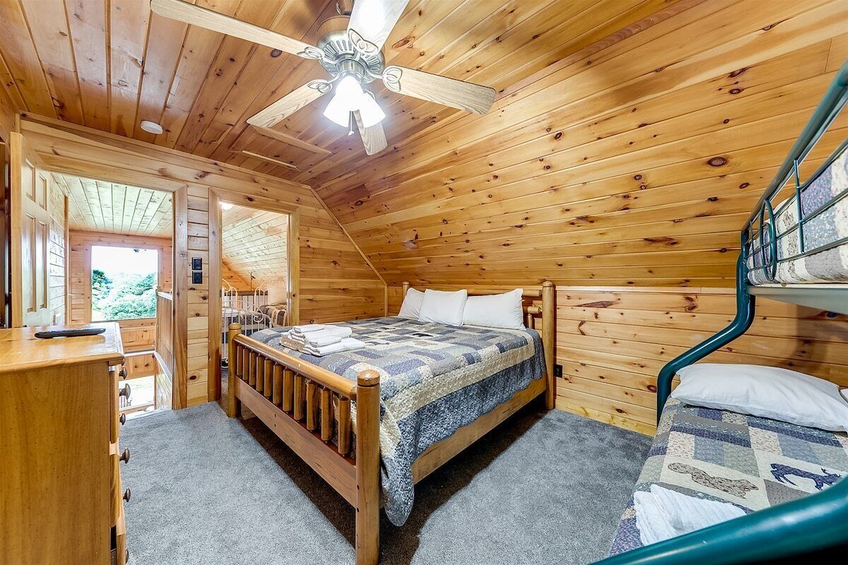 A wooden cabin bedroom with a bed, a desk, and a bunk bed.