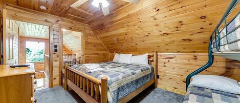 A wooden cabin bedroom with a bed, a desk, and a bunk bed.