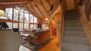 A log cabin interior with a staircase, wooden floors, a sofa, and a dining area.