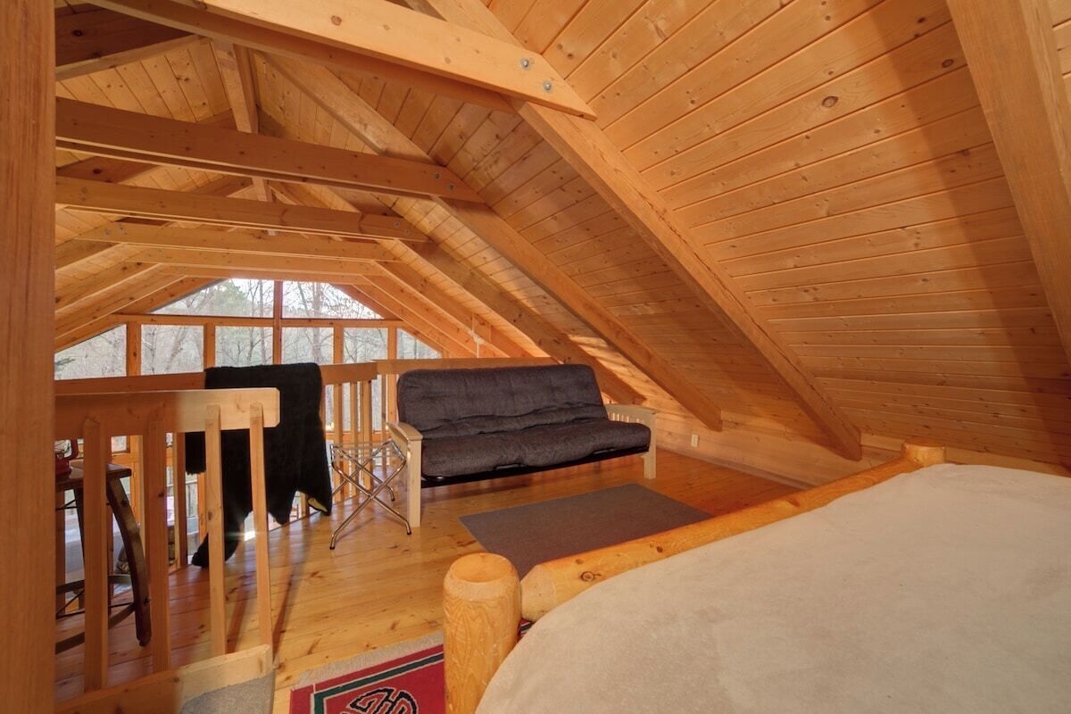Ein gemütliches Schlafzimmer im Dachgeschoss mit Holzbalkendecke, einer Couch und einem Bett.