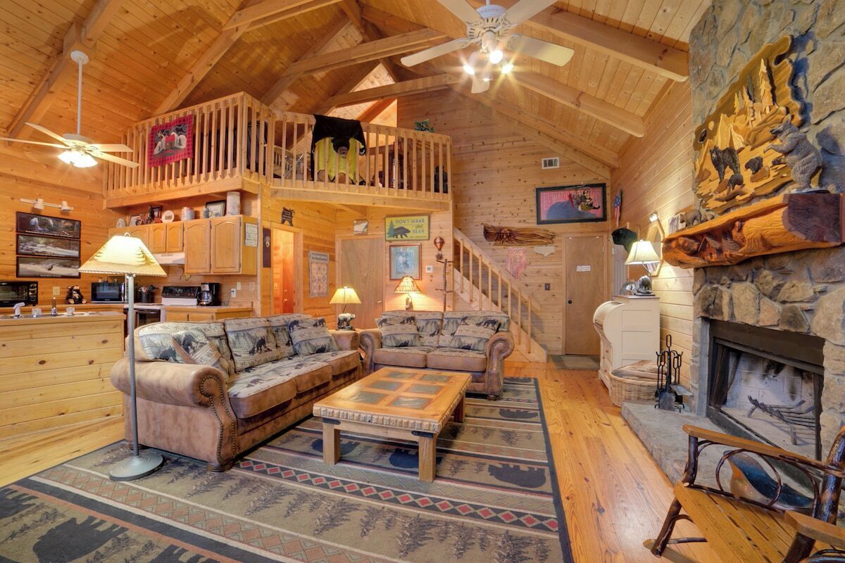 Interior acogedor de una cabaña con habitación en altillo, muebles de madera, chimenea y una pared de acento de piedra.