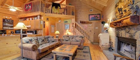 Interior acogedor de una cabaña con habitación en altillo, muebles de madera, chimenea y una pared de acento de piedra.