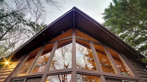 A cabin with a triangular roof, large windows, and a log exterior.