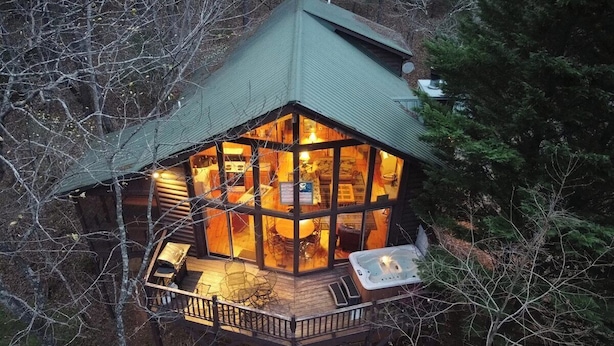 A cabin with a glass enclosure, a hot tub, and a deck.