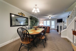 A dining area with a table, chairs, a chandelier, and a staircase.