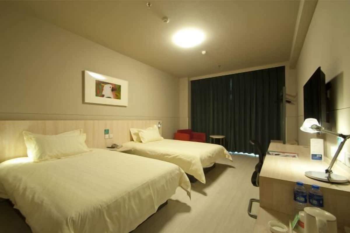 Et hotelværelse med to senge, et skrivebord med lampe, et lille bord og et fjernsyn.