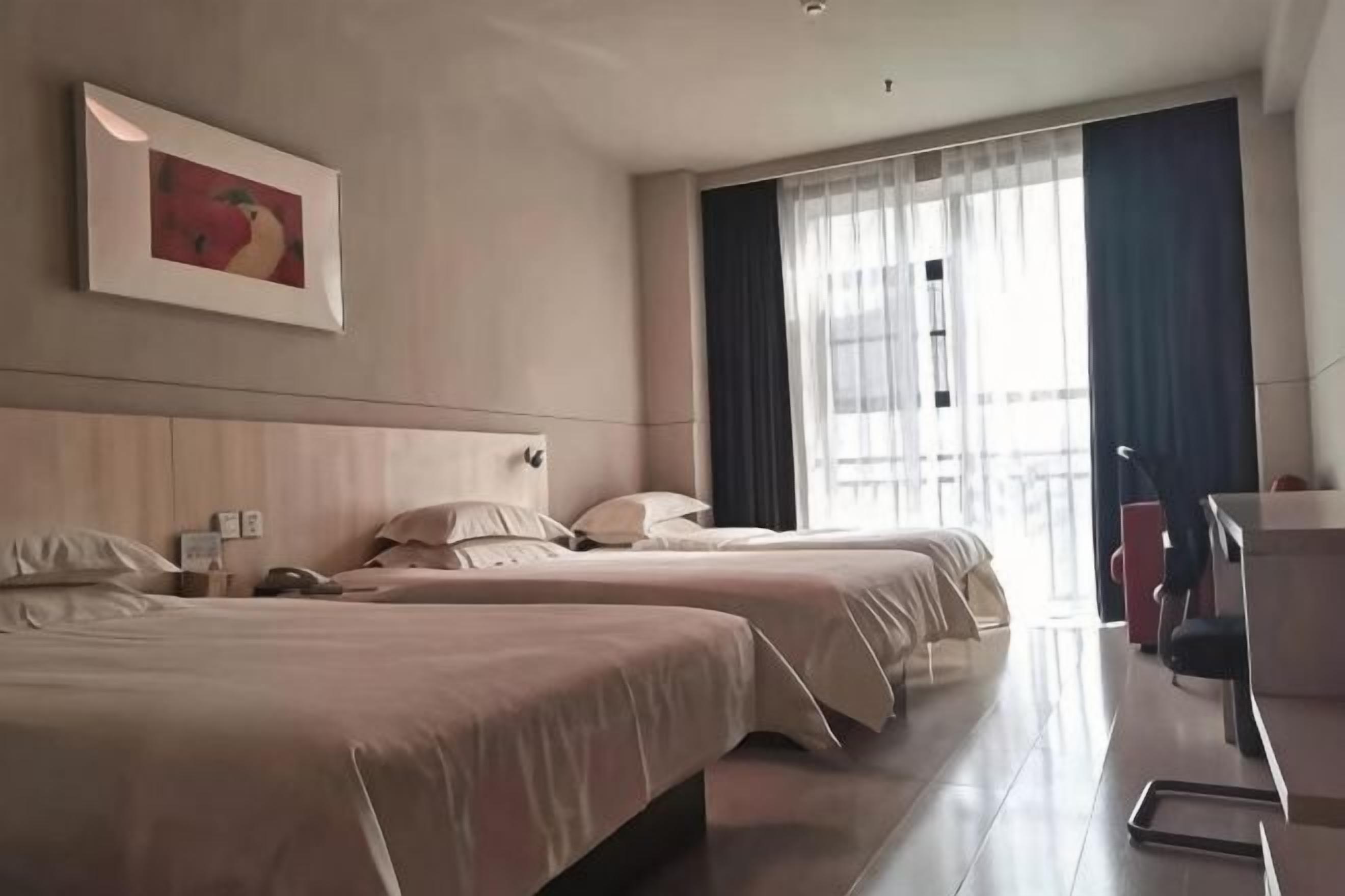 A hotel room with two beds, a desk, a chair, and a large window with curtains.