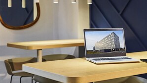 Un intérieur moderne avec un ordinateur portable posé sur une table, des chaises, des luminaires suspendus et un motif géométrique sur le mur.