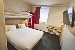 Une chambre d’hôtel avec un lit superposé, un bureau avec une chaise, une télévision et une fenêtre avec des rideaux.