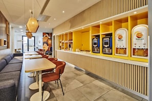 A modern restaurant interior with seating, a counter with beverage dispensers, and a view of the outside. - Kyriad ECO - Clermont Ferrand Estaing (Clermont-Ferrand)