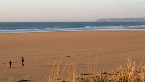 Une vaste plage de sable fin, avec des vagues douces et une falaise qui se dessine à l'horizon.