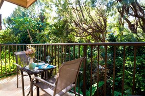 Ein Balkon mit Tisch für zwei Personen, umgeben von üppigem Grün.