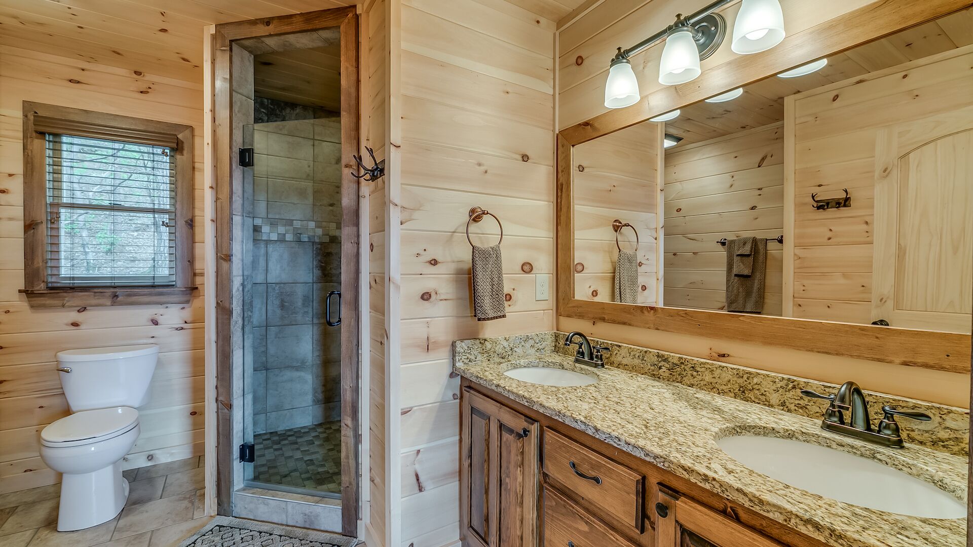 A wooden cabin bathroom with a glass-enclosed shower, a large mirror, and two sinks.