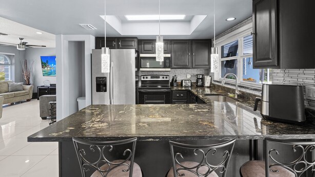 A modern kitchen with a large island, dark cabinets, stainless steel appliances, and pendant lighting. - Stunning Home in Beautiful "Floresta Pines" Port St Lucie! (Port St. Lucie)
