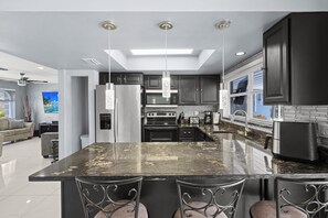 Une cuisine moderne dotée d’un grand îlot central, de meubles de couleur sombre, d’appareils électroménagers en acier inoxydable et de luminaires suspendus.