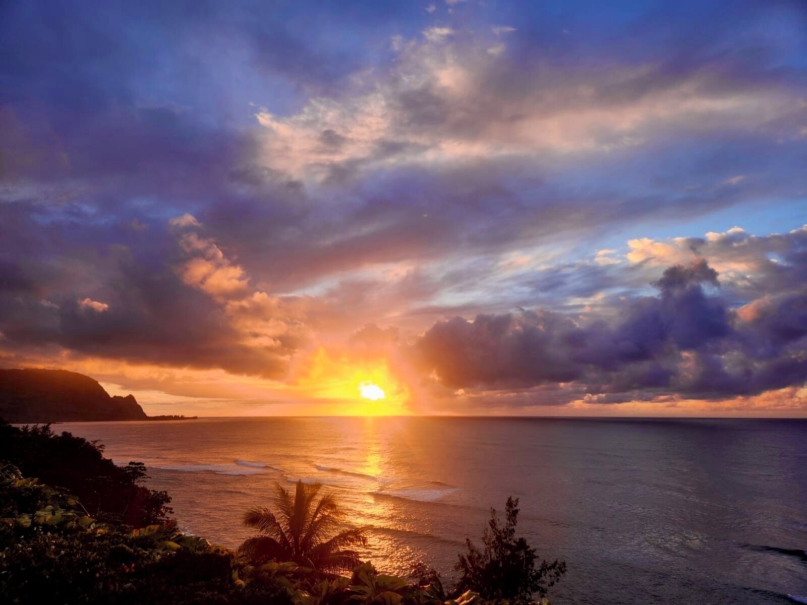 A sunset over the ocean with clouds and a silhouette of a mountain.