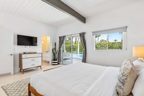 Un dormitorio con cama, televisión, cómoda, ventana con cortinas y vista a una piscina.