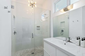 Un baño moderno con ducha de vidrio, un espejo grande y accesorios blancos.