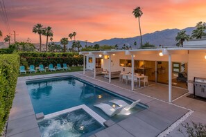 Un área de piscina moderna con sillas de descanso, una bañera de hidromasaje y un patio con mobiliario exterior.