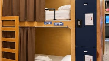 A bunk bed room with a ladder, a desk, and a computer. There are signs indicating room numbers and a door with an exit sign.
