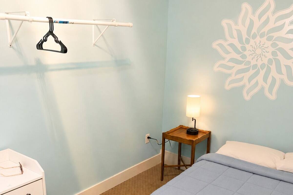 A bedroom with a bed, a nightstand, a lamp, a dresser, and a wall decoration.