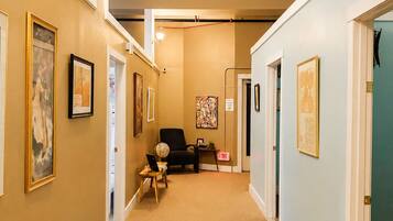 A hallway with beige walls, framed artwork, a black chair, and a desk with a laptop.