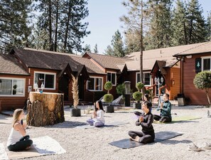 A group of people practicing yoga outdoors in a wooded area with wooden cabins in the background. - Grand Pine Cabins (Wrightwood)
