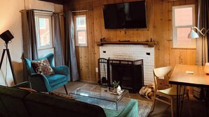 Una sala de estar acogedora con chimenea, un televisor de pantalla plana montado arriba y un espacio de descanso cómodo con un sofá y sillones.