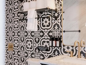 A bathroom with a black and white patterned wall, a towel rack with a white towel, a sink with a gold faucet, and a sign instructing not to flush anything except toilet paper. - Grand Pine Cabins (Wrightwood)